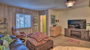 A living room with a leather sofa, a recliner, a patterned ottoman, a wooden entertainment center, and a ceiling fan.