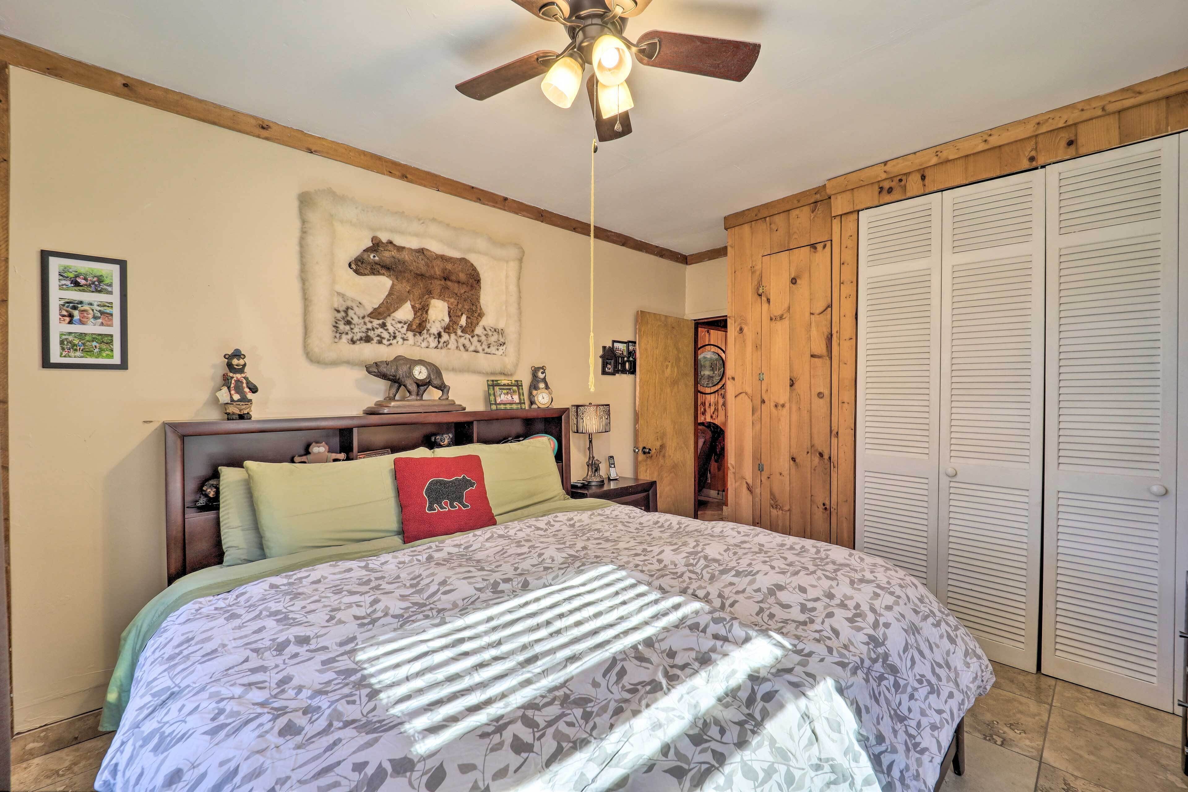 A bedroom with a bed, a ceiling fan, a wooden wardrobe, and a wall-mounted picture.