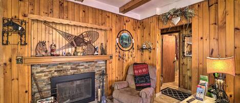 Una habitación acogedora con chimenea, paredes de madera, un sillón cómodo y una pequeña mesa con lámpara.