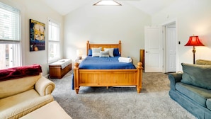 A bedroom with a wooden bed, a beige sofa, a blue armchair, a red lamp, and a poster on the wall. - Walk to Walnut St: Pet-friendly Pittsburgh Home! (Pittsburgh)