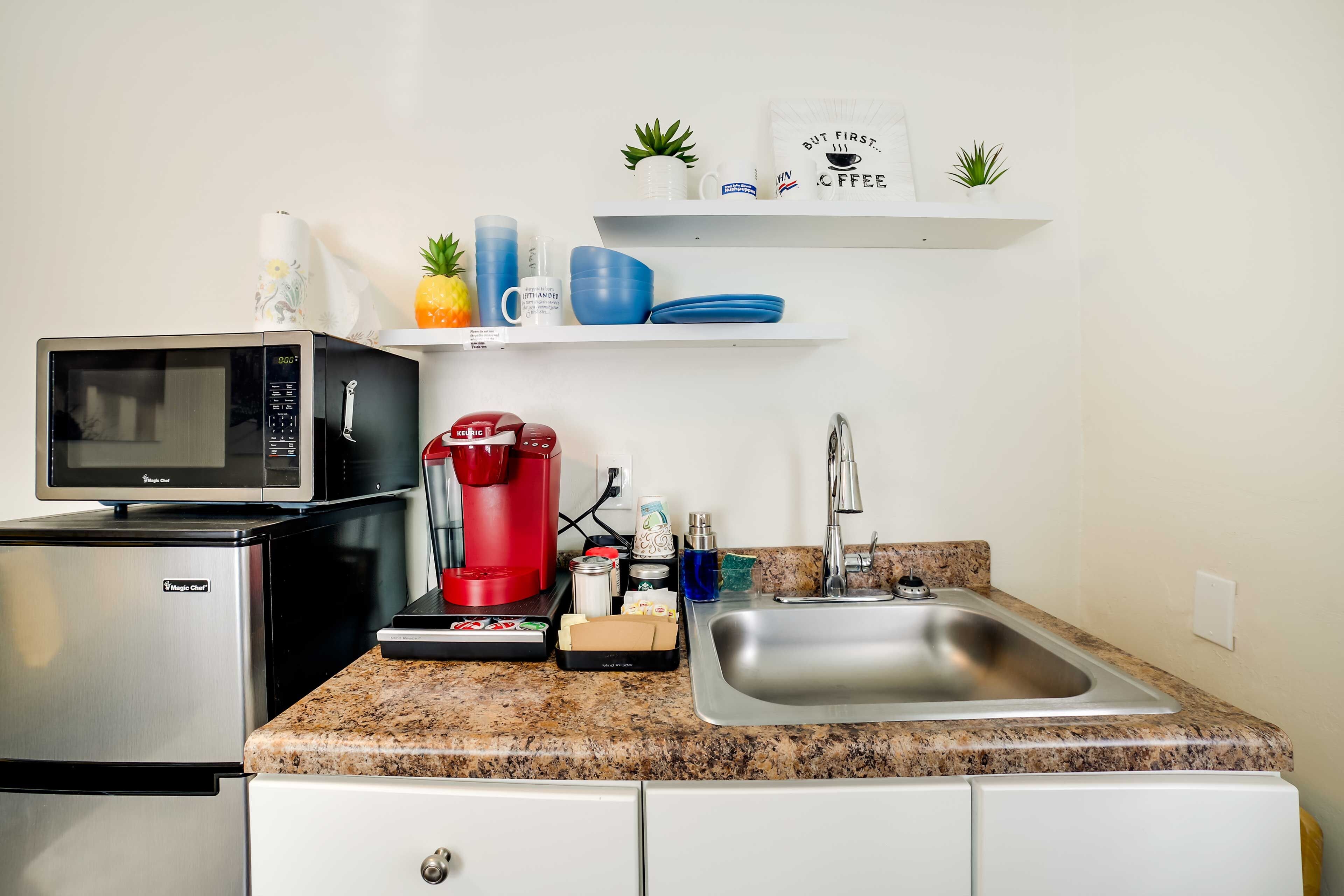 A compact kitchen with a microwave, coffee maker, and stainless steel sink.