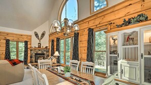 L’intérieur d’un chalet confortable, avec une table à manger, des chaises, une cheminée et de grandes fenêtres.