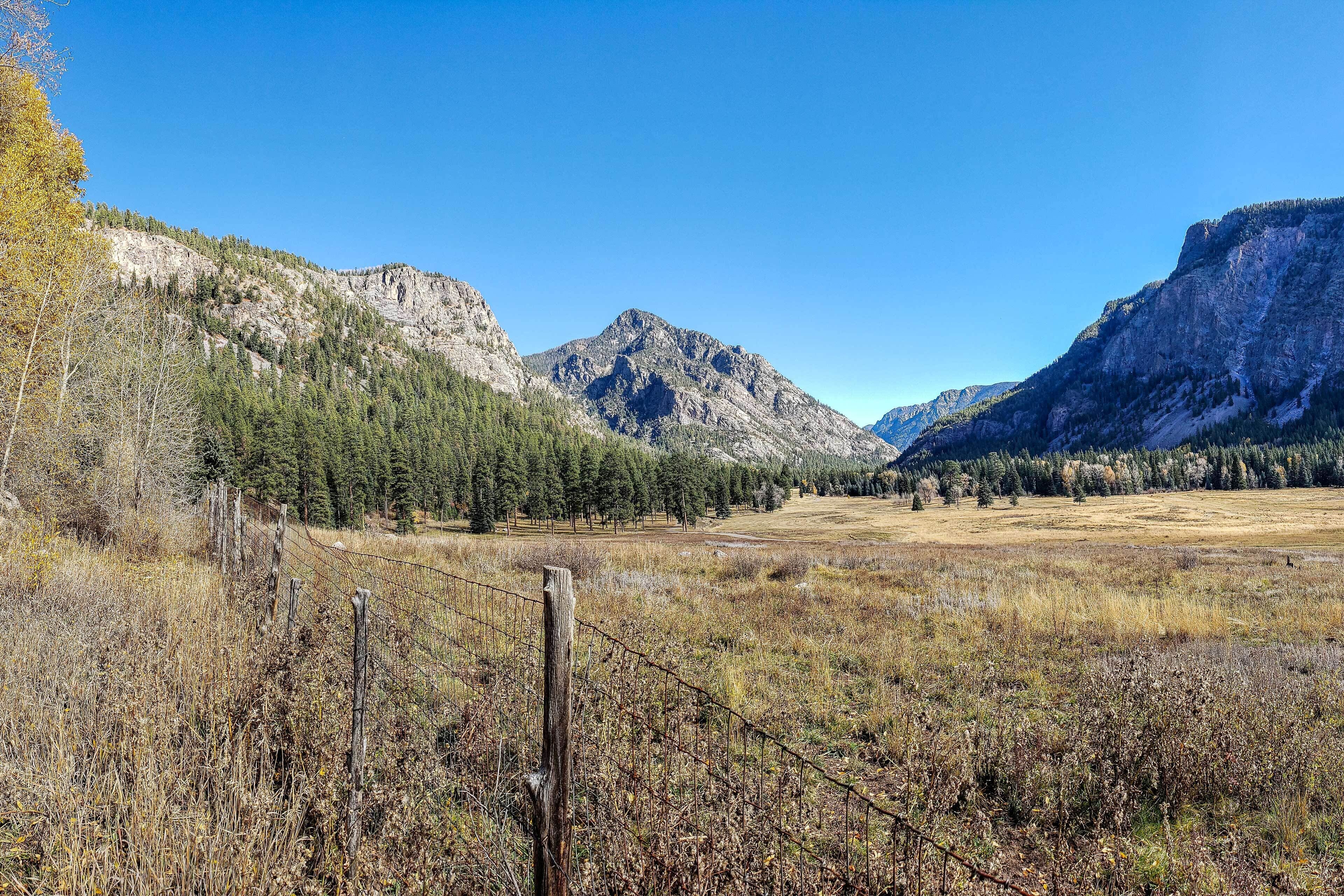A mountainous landscape with a grassy field and a wooden fence.