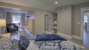 A bedroom with a large bed, a chair, a desk, and a window.