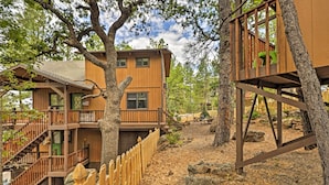 A multi-story wooden cabin with a wooden deck and staircase, surrounded by trees and a natural landscape. - Pet-friendly Munds Park Retreat w/ Wraparound Deck (Munds Park)