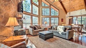 A spacious living room with large windows, a stone wall, and a wooden ceiling. - Pet-friendly Munds Park Retreat w/ Wraparound Deck (Munds Park)