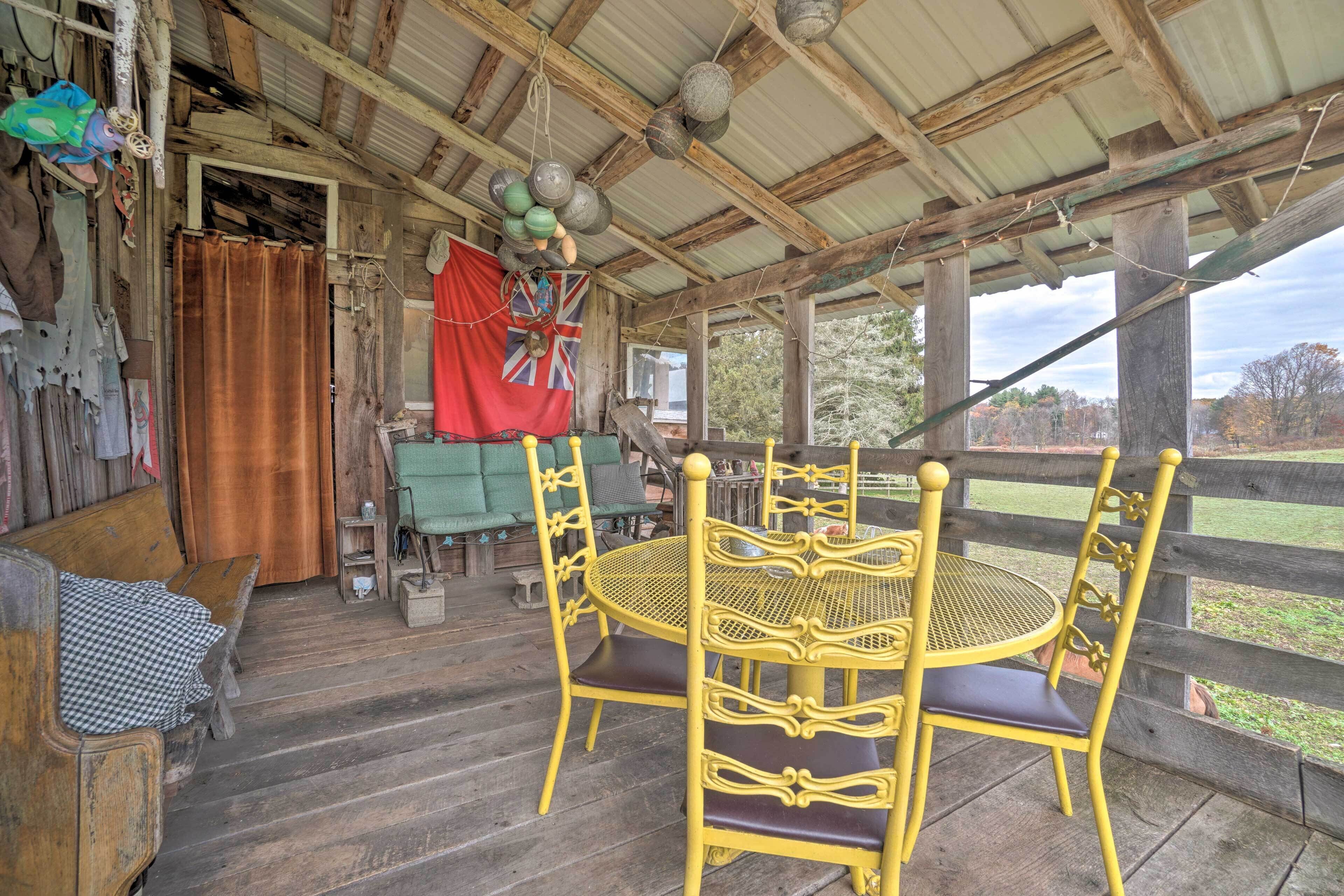 Une véranda en bois rustique, avec une table ronde jaune et des chaises assorties, un drapeau rouge et une vue sur l’extérieur.