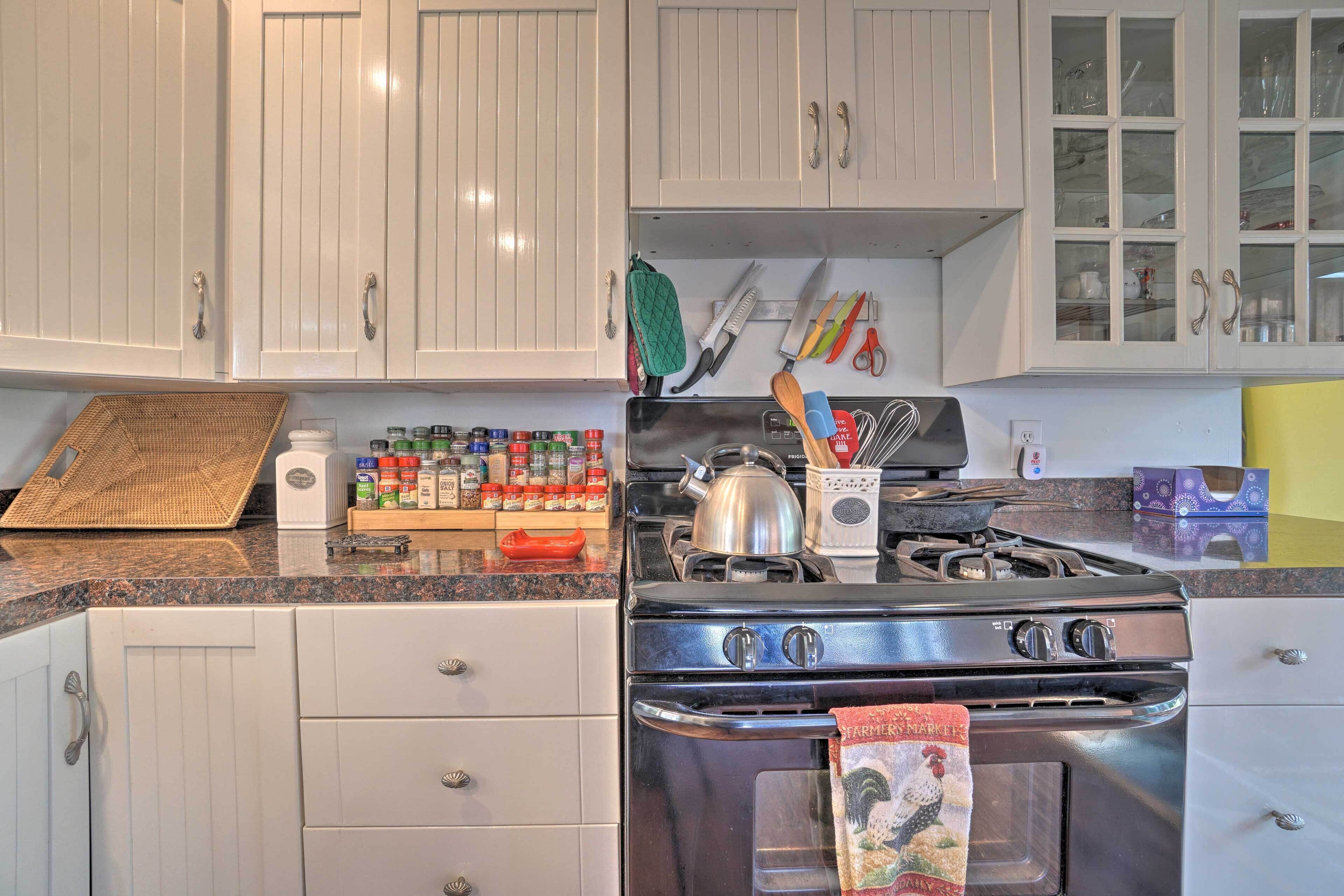 A kitchen with white cabinets, a stove, and various cooking utensils.