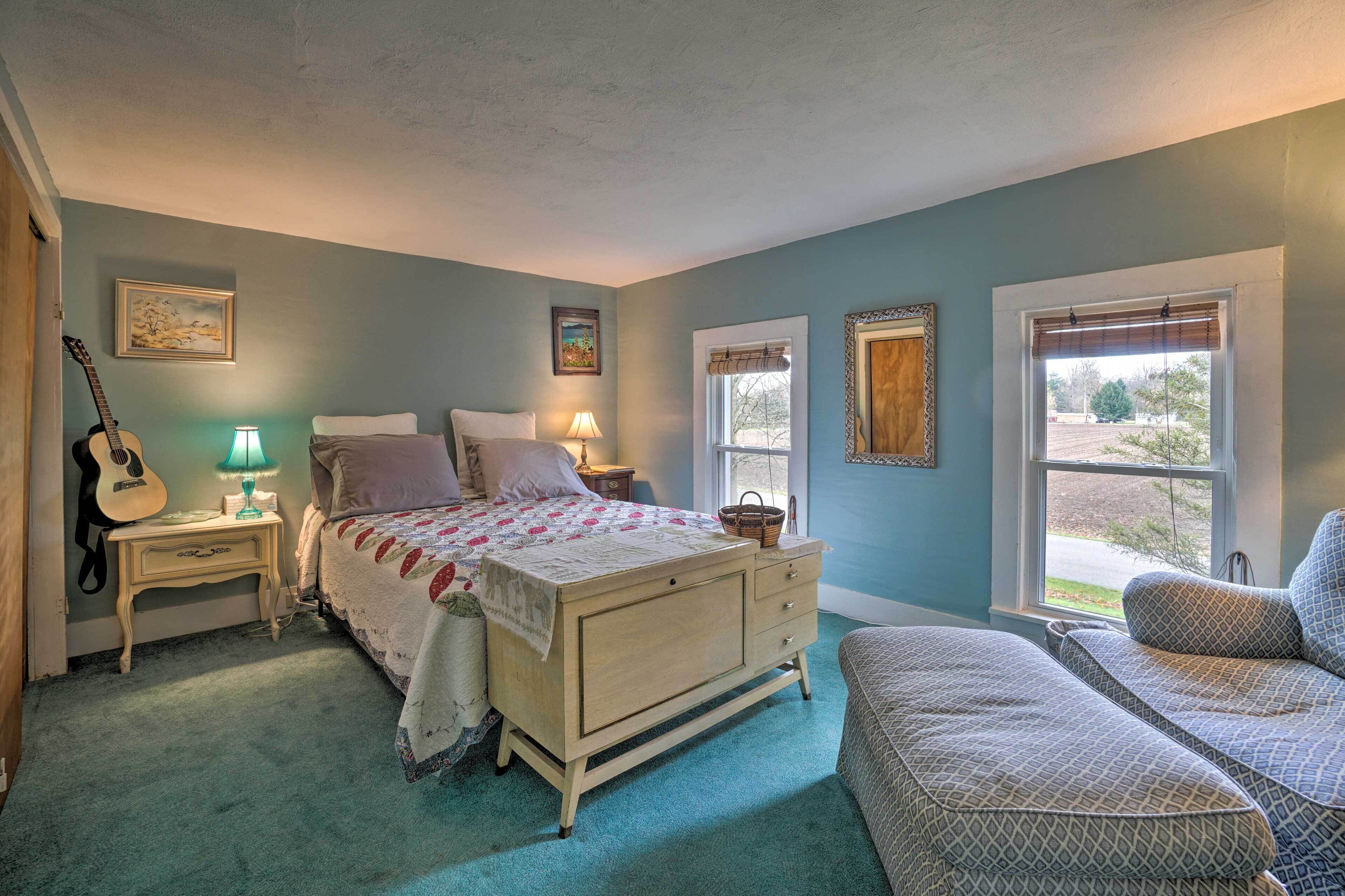 A bedroom with a bed, bedside tables, a lamp, a guitar, and a window with a view.