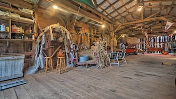A rustic barn interior with wooden floors, metal shelving, and various farming equipment.