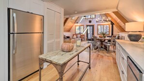 A kitchen with a stainless steel refrigerator, a rustic wooden table with a pumpkin and a glass of milk, and a dining area with a chandelier and a large window. - Deck & Forest Views: Munds Park A-frame Cabin (Munds Park)