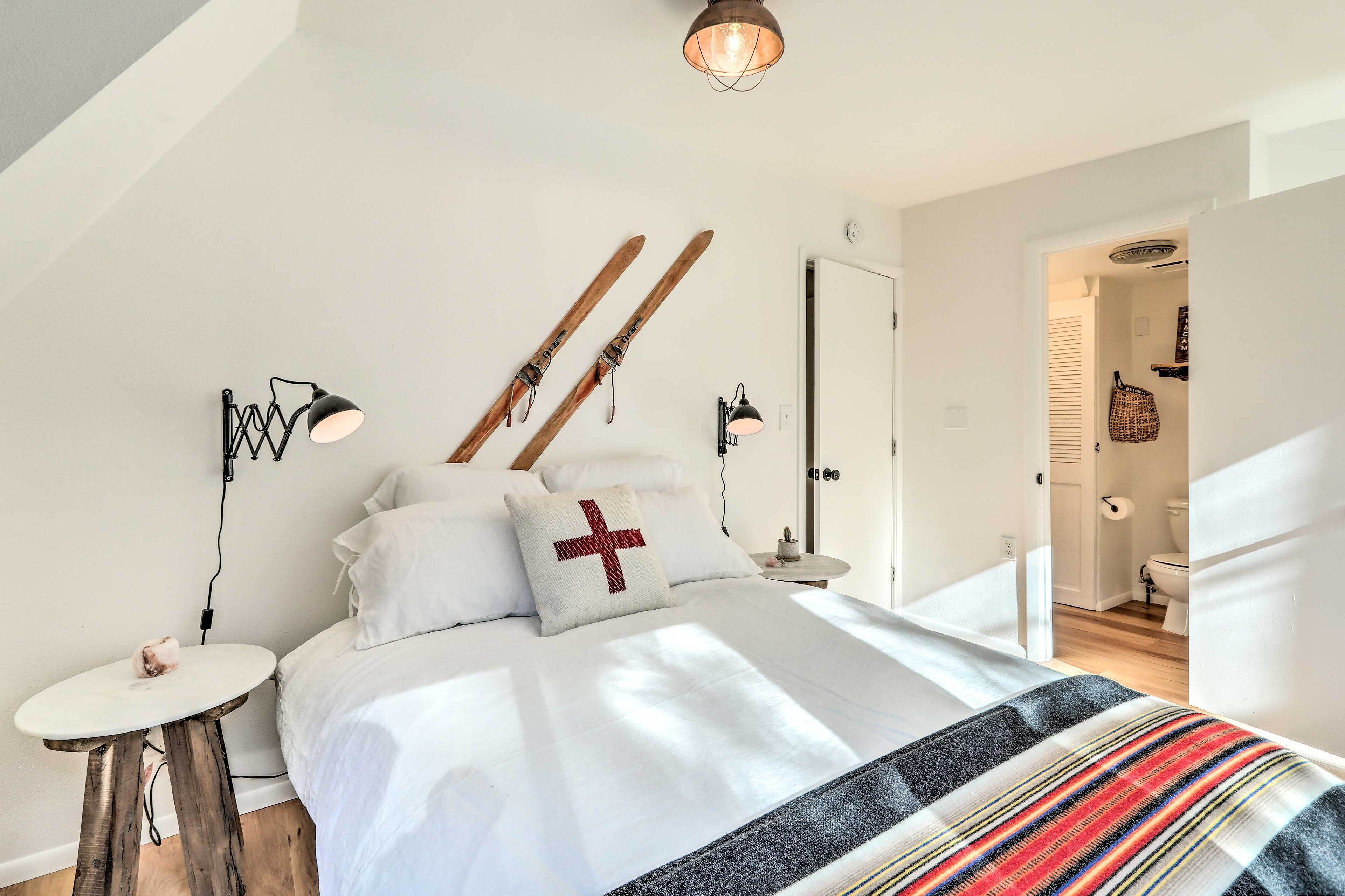 A bedroom with a bed, skis leaning against the wall, a small round table, and a lamp.