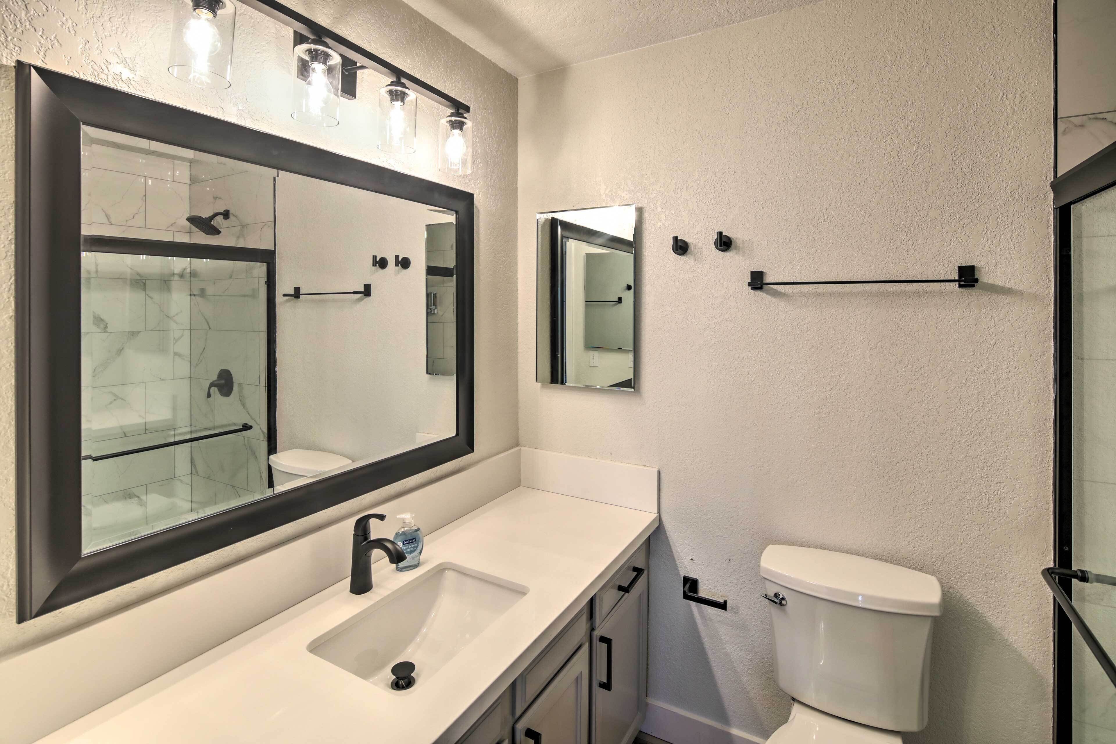 A modern bathroom with a large mirror, a sink, a toilet, and a shower.