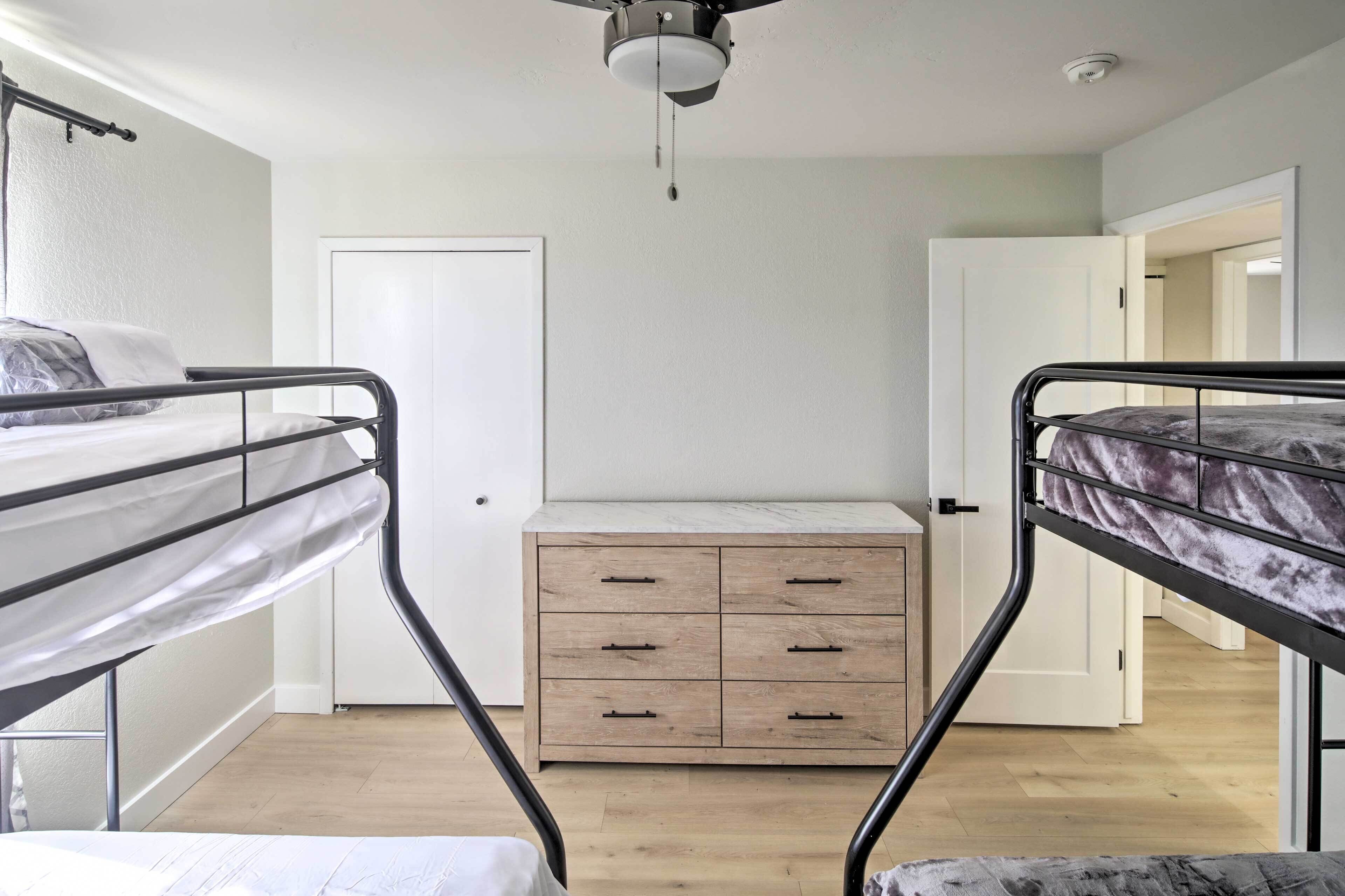 A bedroom with two bunk beds, a wooden dresser, and a ceiling fan.