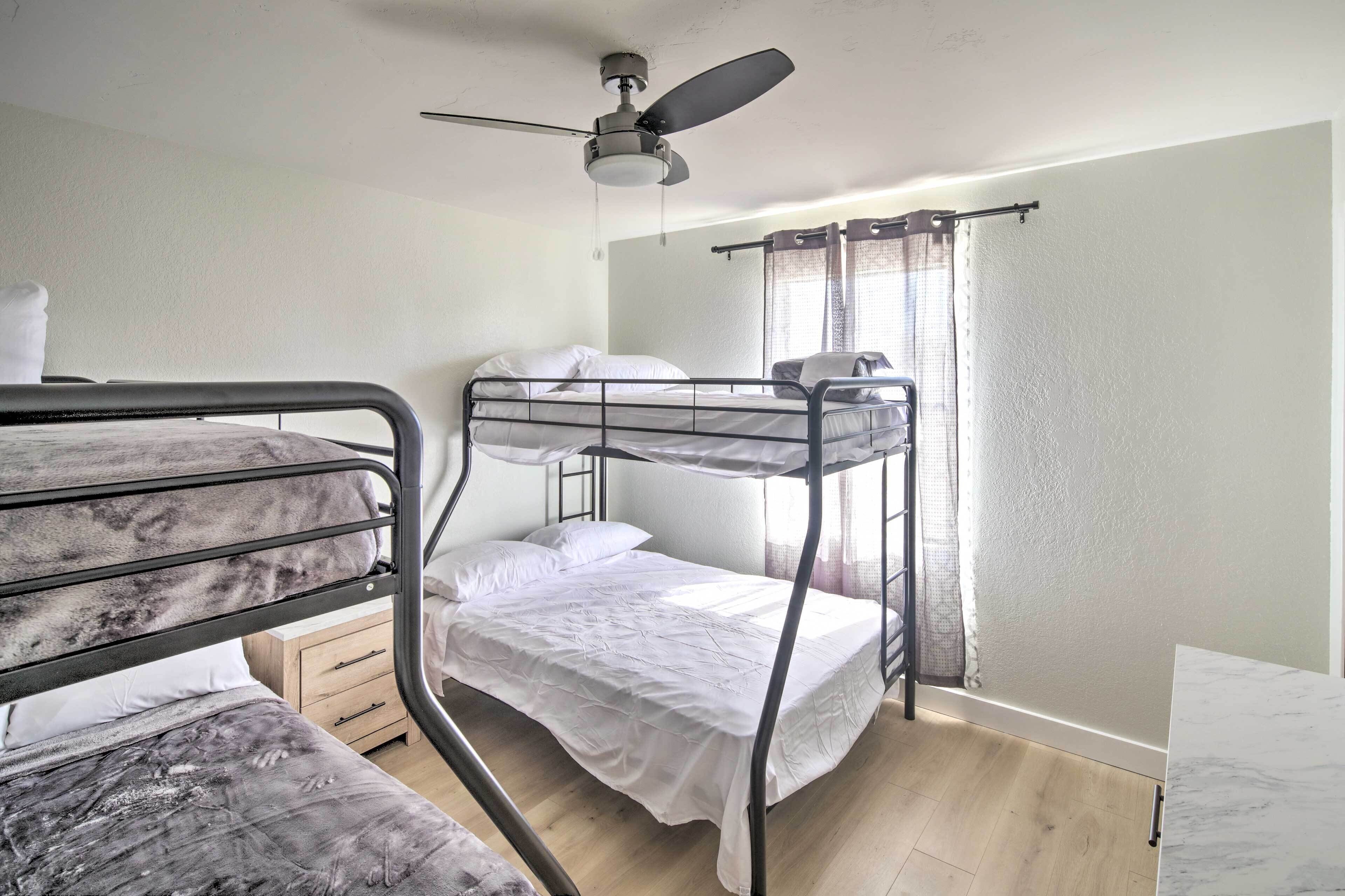 Une chambre avec un lit superposé, un ventilateur de plafond, une petite armoire en bois et une fenêtre avec des rideaux.