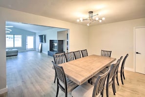 Een ruime eethoek met een houten tafel en stoelen, een moderne kroonluchter, en zicht op de woonkamer.