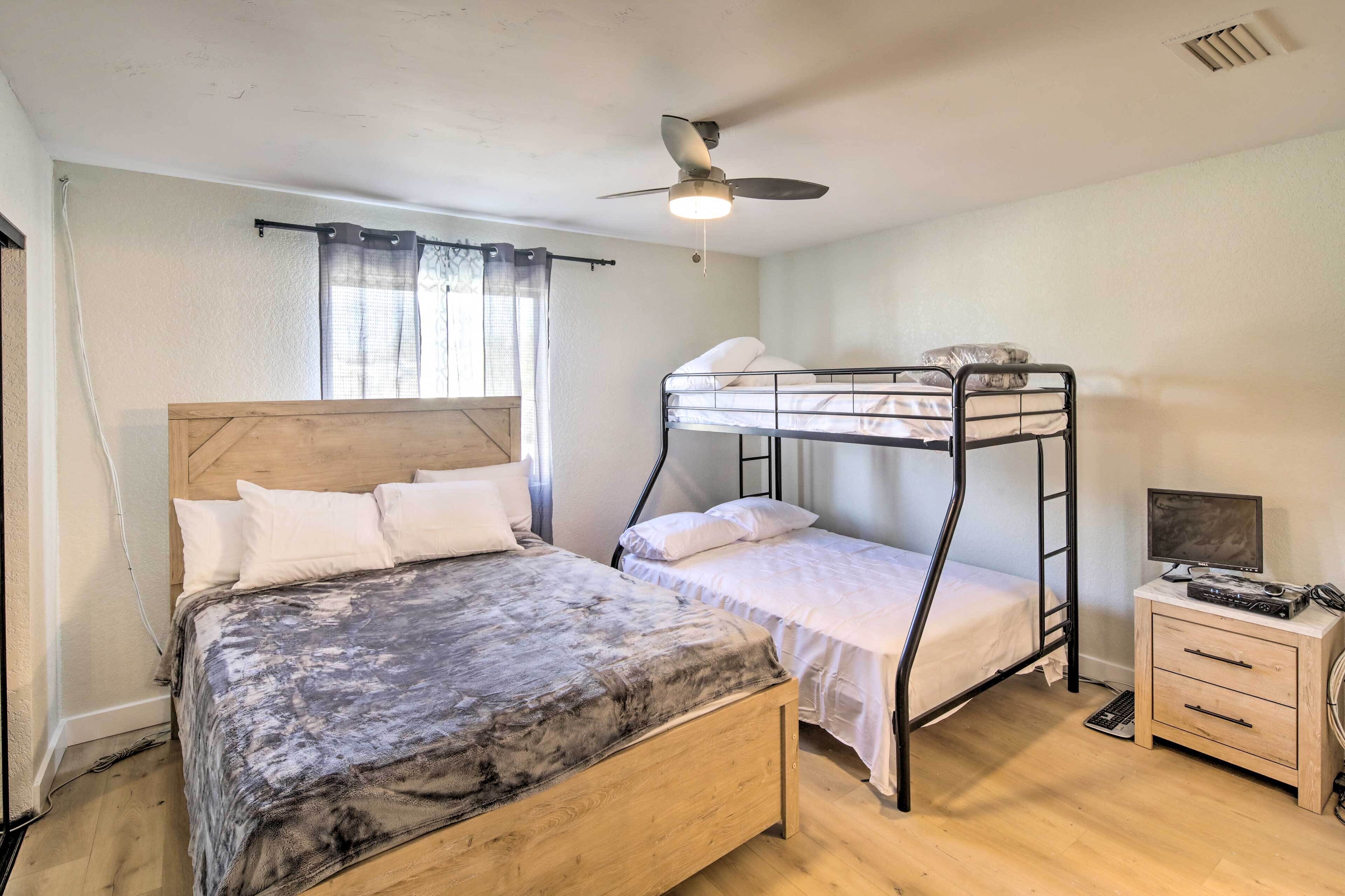 Une chambre avec un lit en bois, un lit superposé, un ventilateur de plafond, une fenêtre avec des rideaux et une petite table de chevet avec un téléviseur.