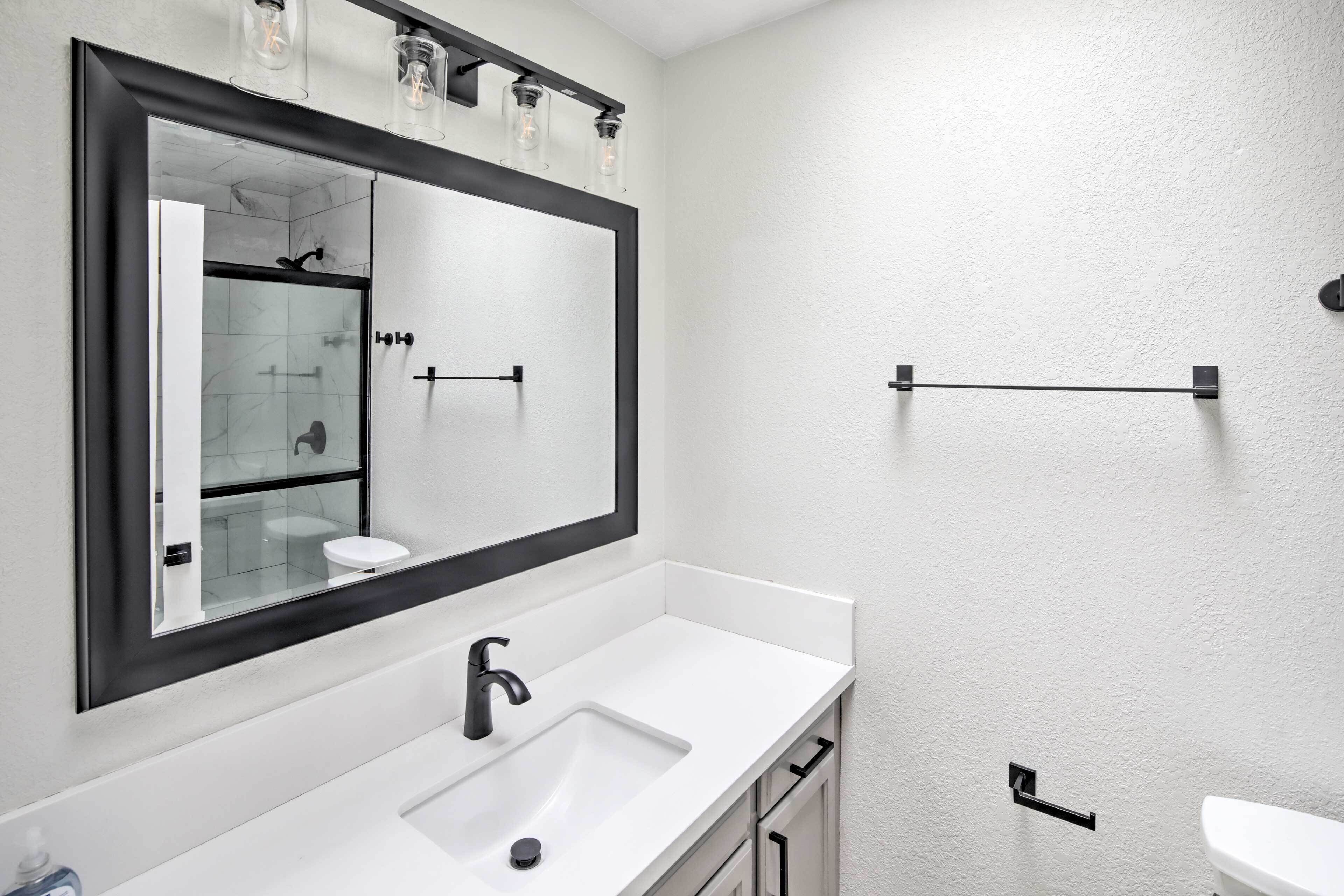 A modern bathroom with a large mirror, a white sink, and a black faucet.