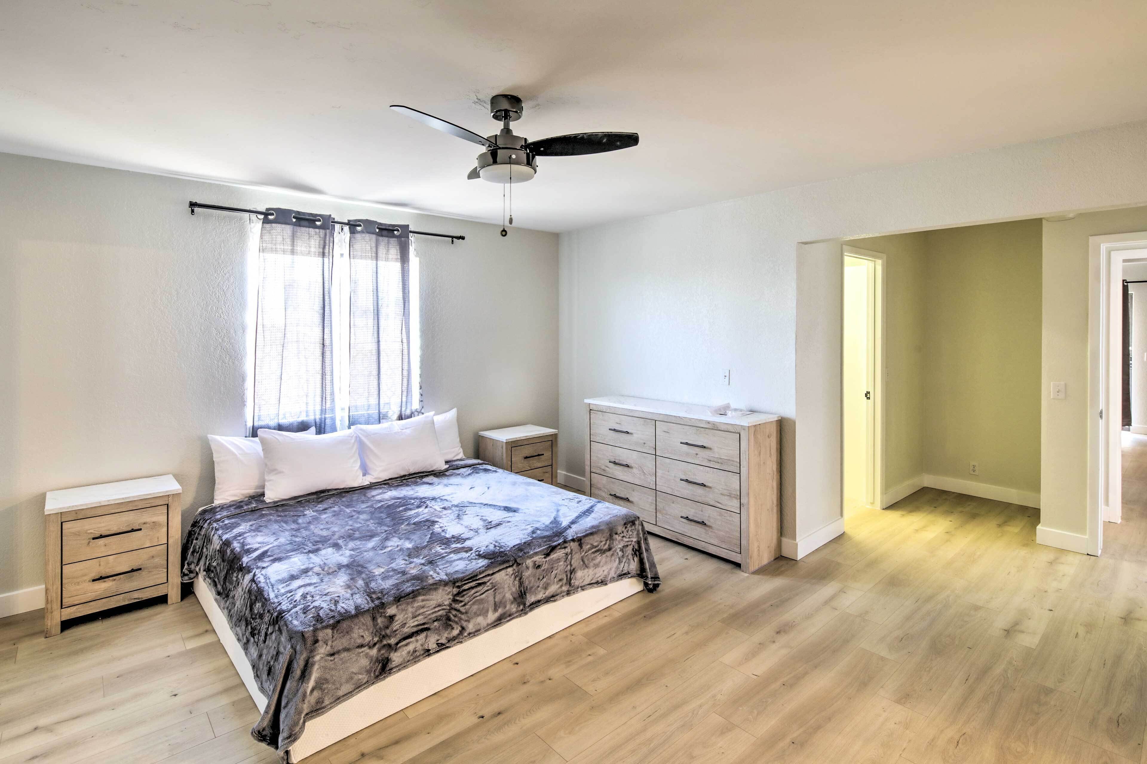 Een slaapkamer met een bed, nachtkastje, dressoir, plafondventilator en een raam met gordijnen.