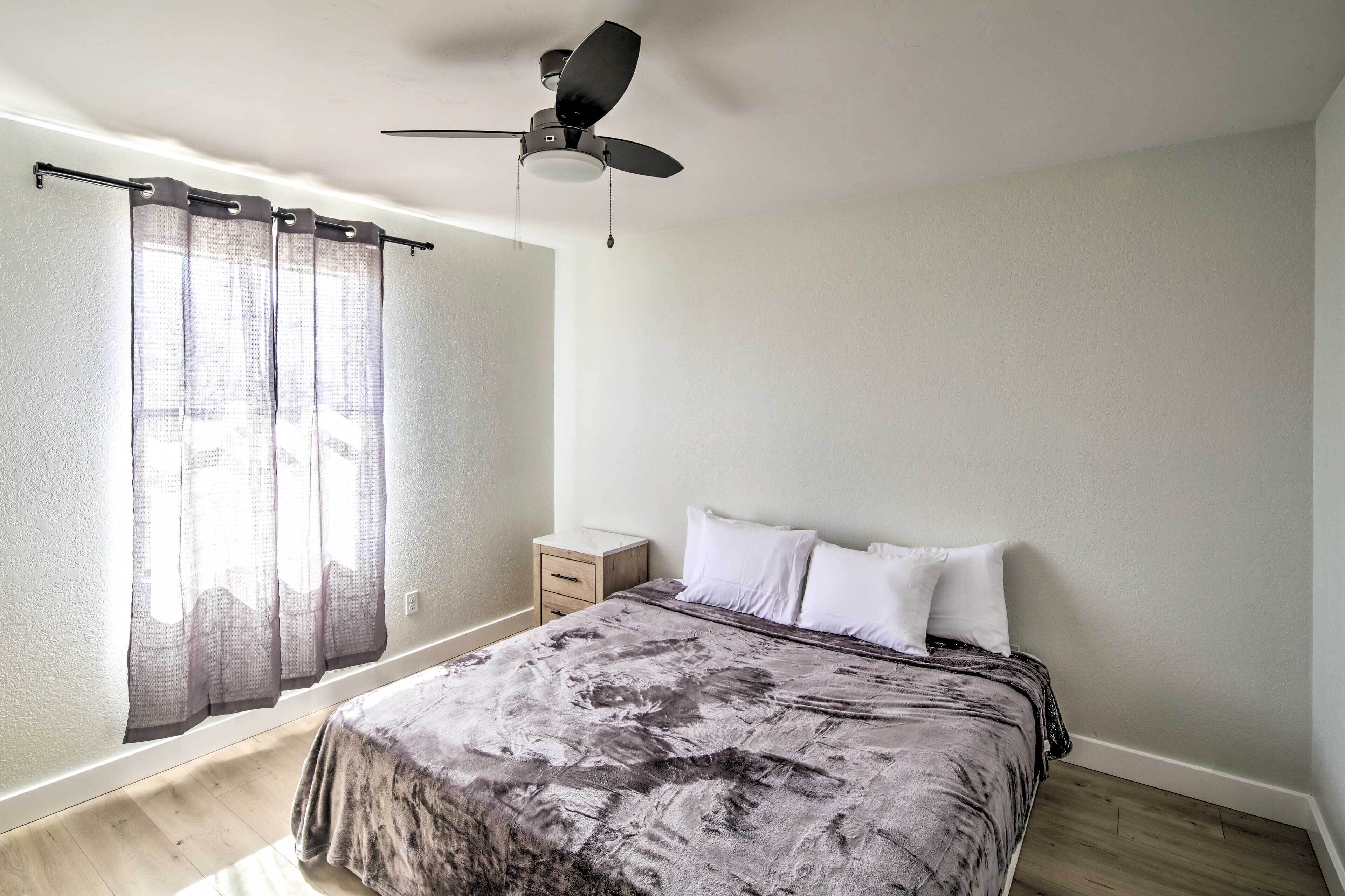 Ein Schlafzimmer mit einem Bett, einem Nachttisch, einem Deckenventilator und transparenten Vorhängen.