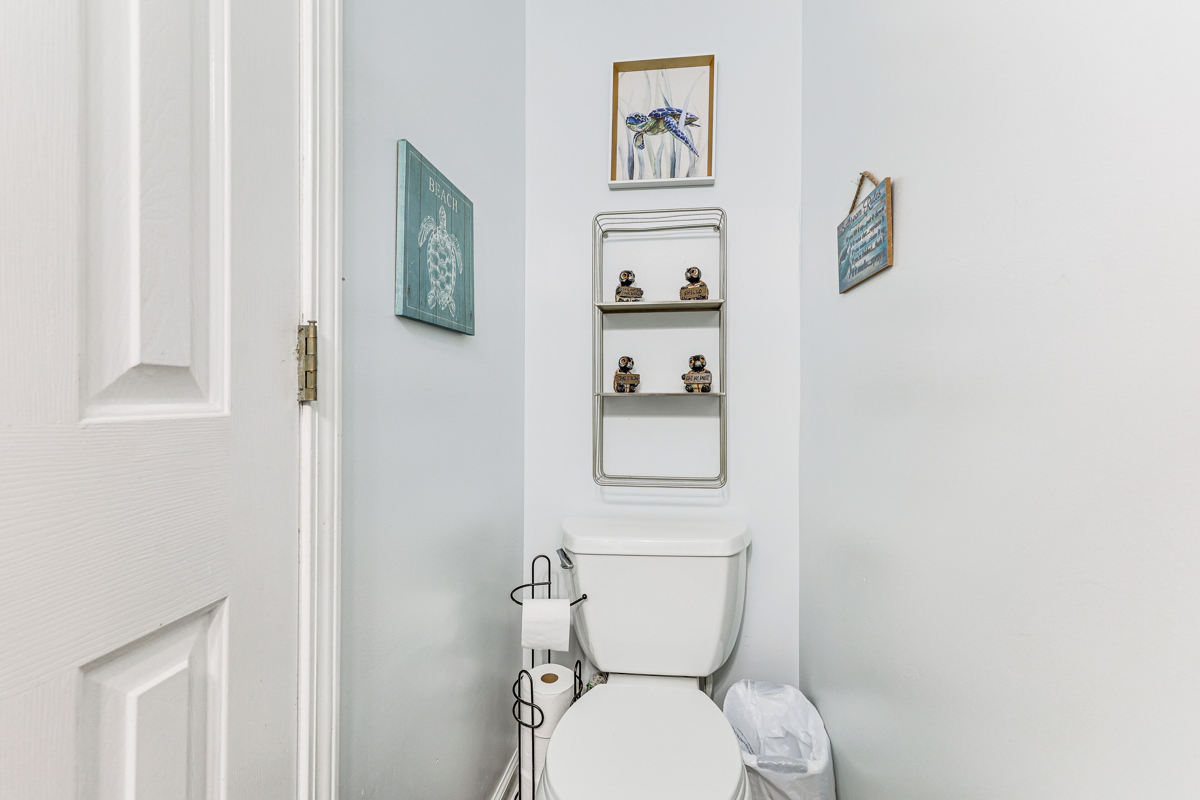 Een badkamer met een toilet, een plank met decoratieve spullen en twee ingekaderde foto's aan de muur.