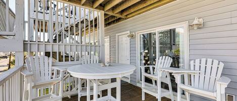 A covered outdoor area with a wooden deck, white Adirondack chairs, and a round table.