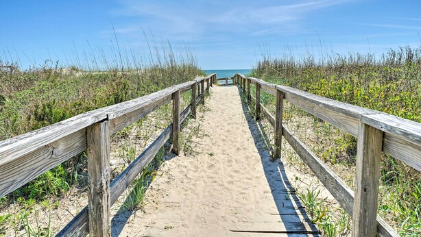 Ein Holzsteg führt zu einem Strand bei blauem Himmel.