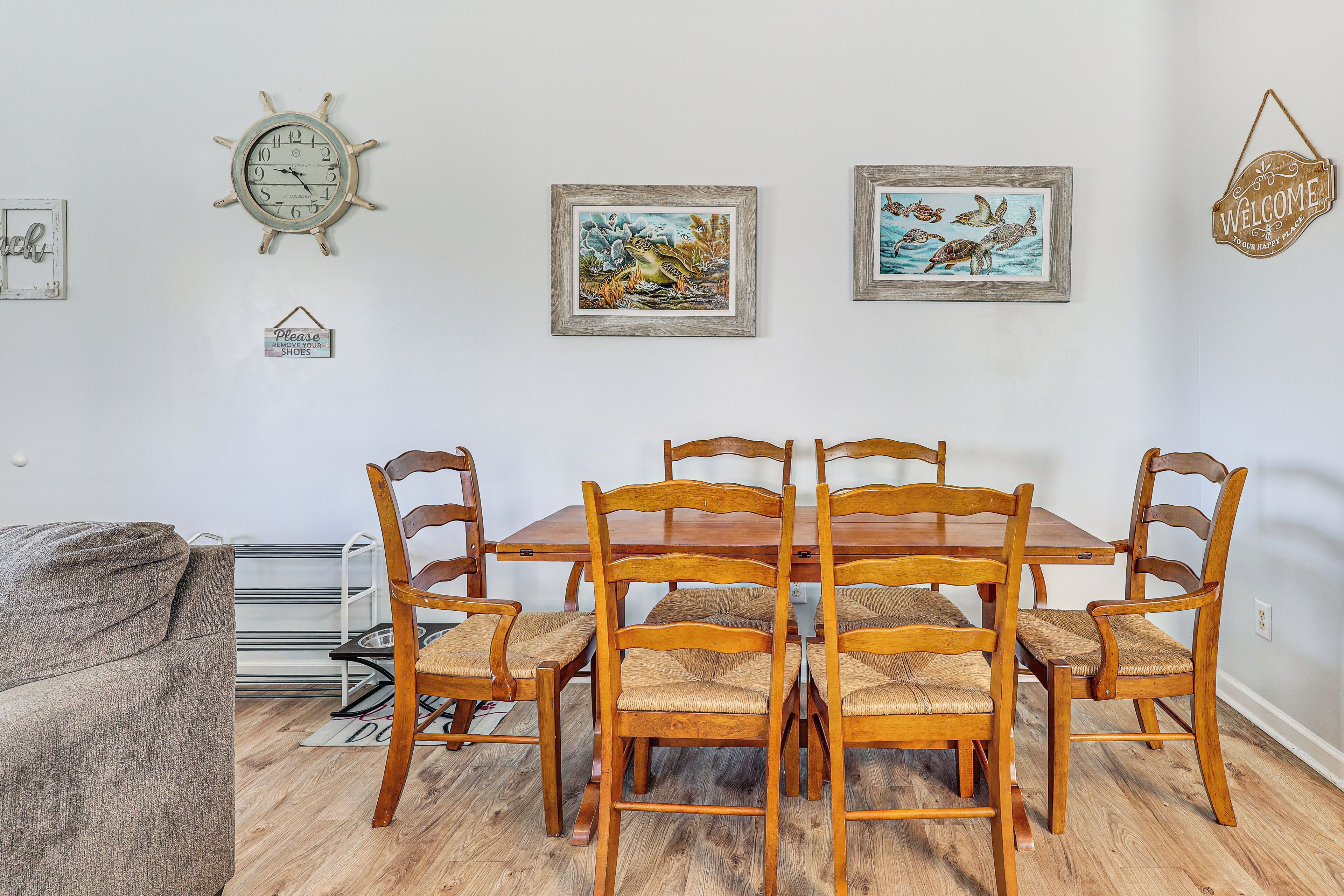 Un comedor con una mesa y sillas de madera, una obra de arte enmarcada en la pared y un reloj.