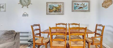 Un comedor con una mesa y sillas de madera, una obra de arte enmarcada en la pared y un reloj.