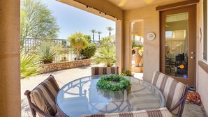 Une terrasse couverte avec une table en verre, des chaises rembourrées et un ventilateur de plafond.