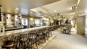 Un grand espace bar doté d’un long comptoir et de nombreux tabourets, d’un téléviseur fixé au mur et offrant une vue dégagée sur le bar.