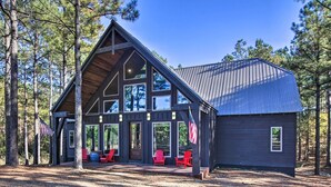 Une cabane dotée d’une grande véranda, de chaises Adirondack rouges et d’un drapeau américain.
