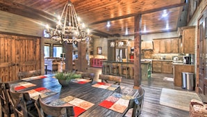 Un intérieur rustique en bois, avec une grande table à manger, des chaises en bois, un lustre et un coin cuisine.