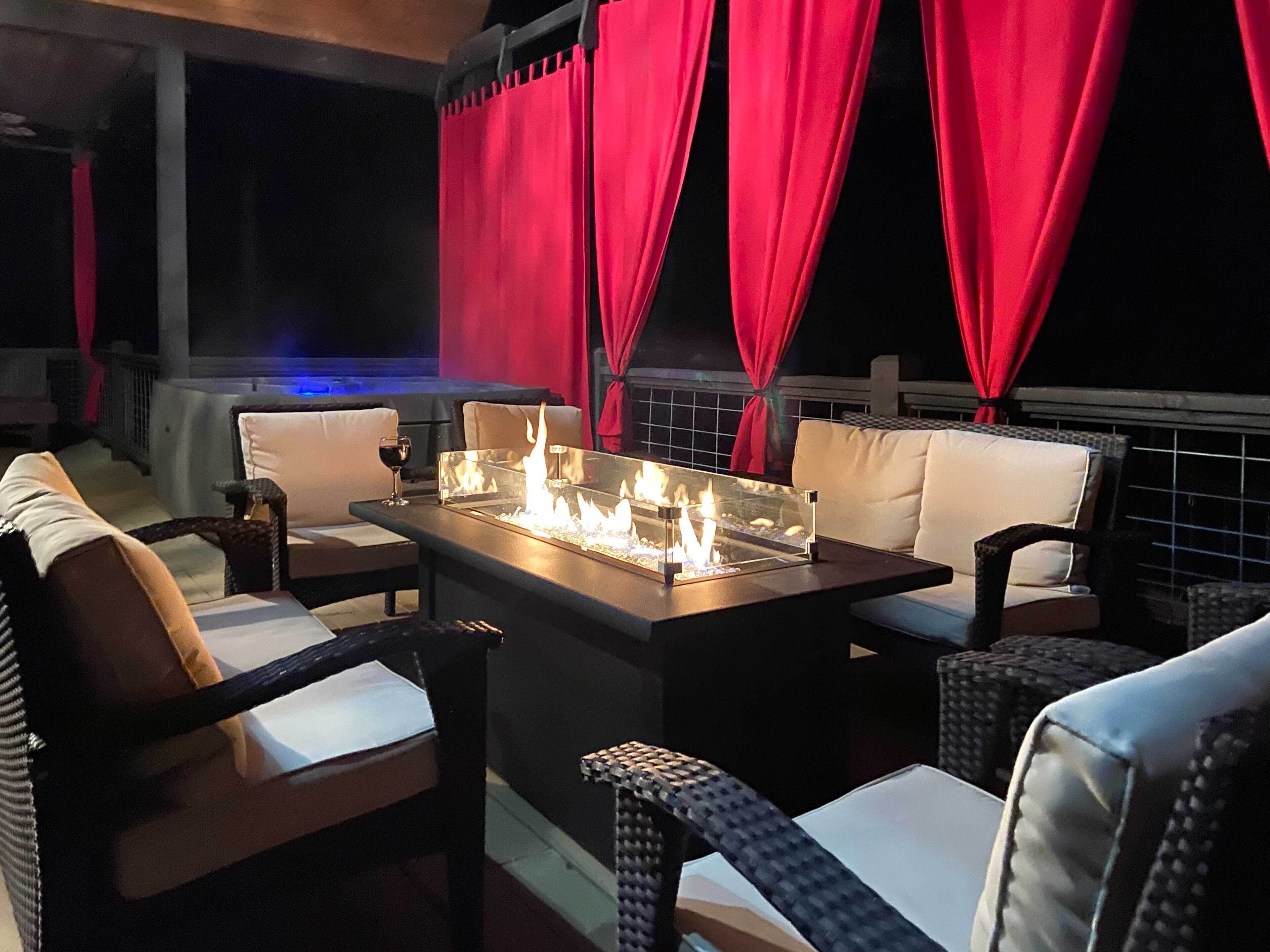 An outdoor seating area with wicker furniture and a glass-top table with a built-in fire feature.