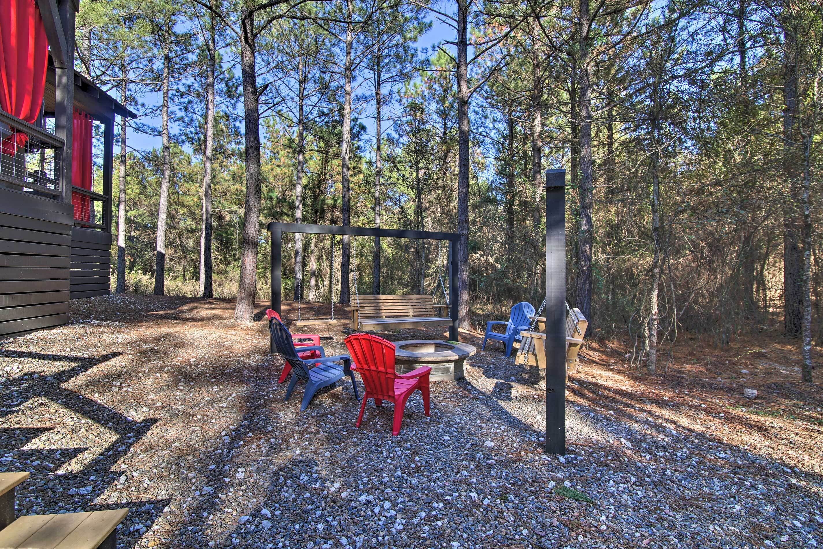 A rustic outdoor seating area with Adirondack chairs, a fire pit, and a wooden bench.