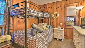 Ein Stockbett mit gemusterten Bettbezügen, ein Nachttisch mit Lampe, eine kleine Kommode und ein Willkommensschild.