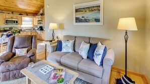 A living room with a sofa, armchair, coffee table, and lamps. There is a kitchen in the background with a microwave and cabinets. - Waterfront Prospect Harbor Cottage: Yard, Fire Pit (Prospect Harbor)