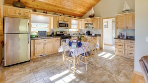 A spacious kitchen with wooden cabinets, a stainless steel refrigerator, a microwave, and a dining table with chairs. - Waterfront Prospect Harbor Cottage: Yard, Fire Pit (Prospect Harbor)