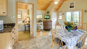 A spacious room with a wooden ceiling, a dining table with a patterned tablecloth, and a television in the background. - Waterfront Prospect Harbor Cottage: Yard, Fire Pit (Prospect Harbor)