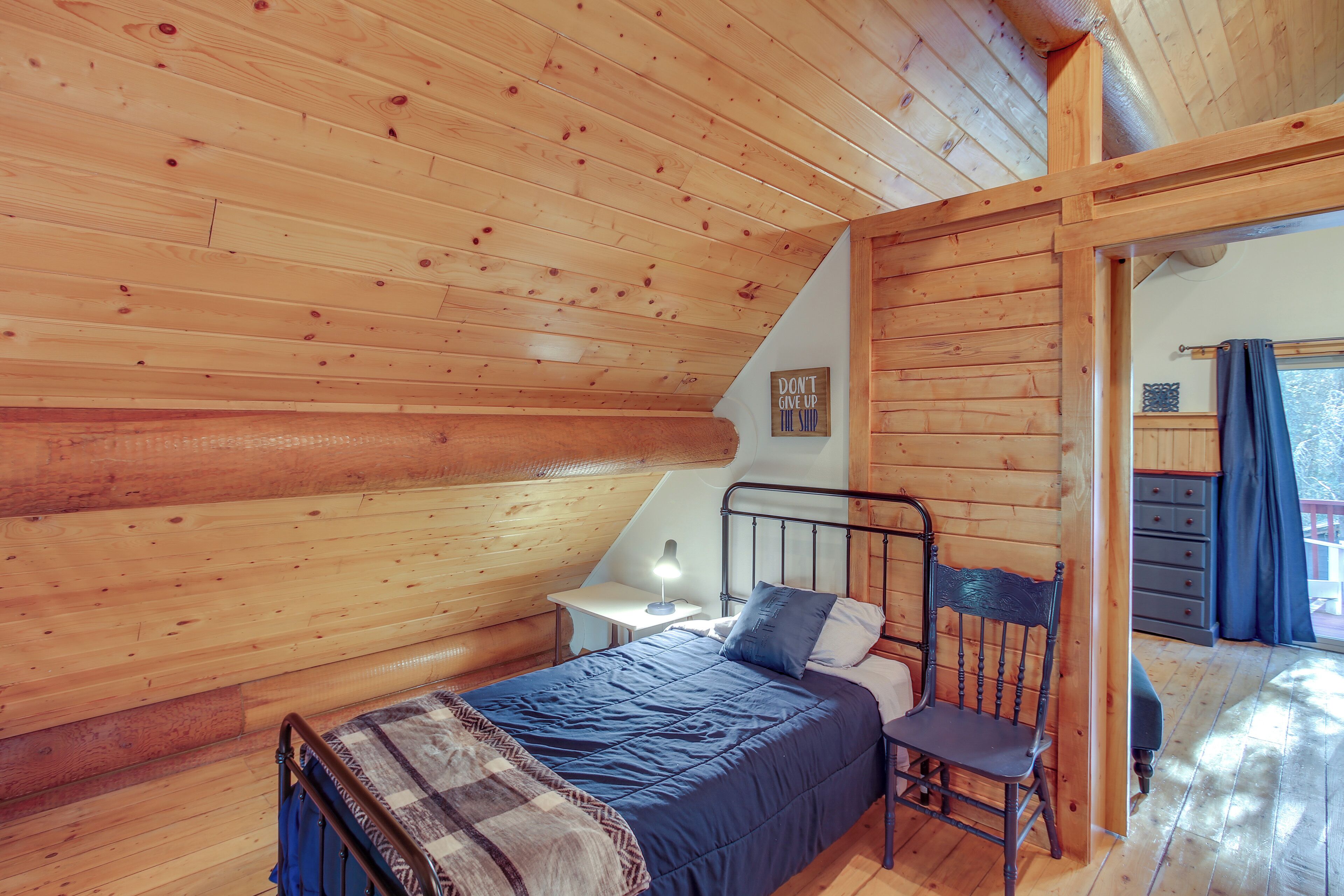 A cozy cabin bedroom with a bed, a chair, a nightstand, and a window with curtains.