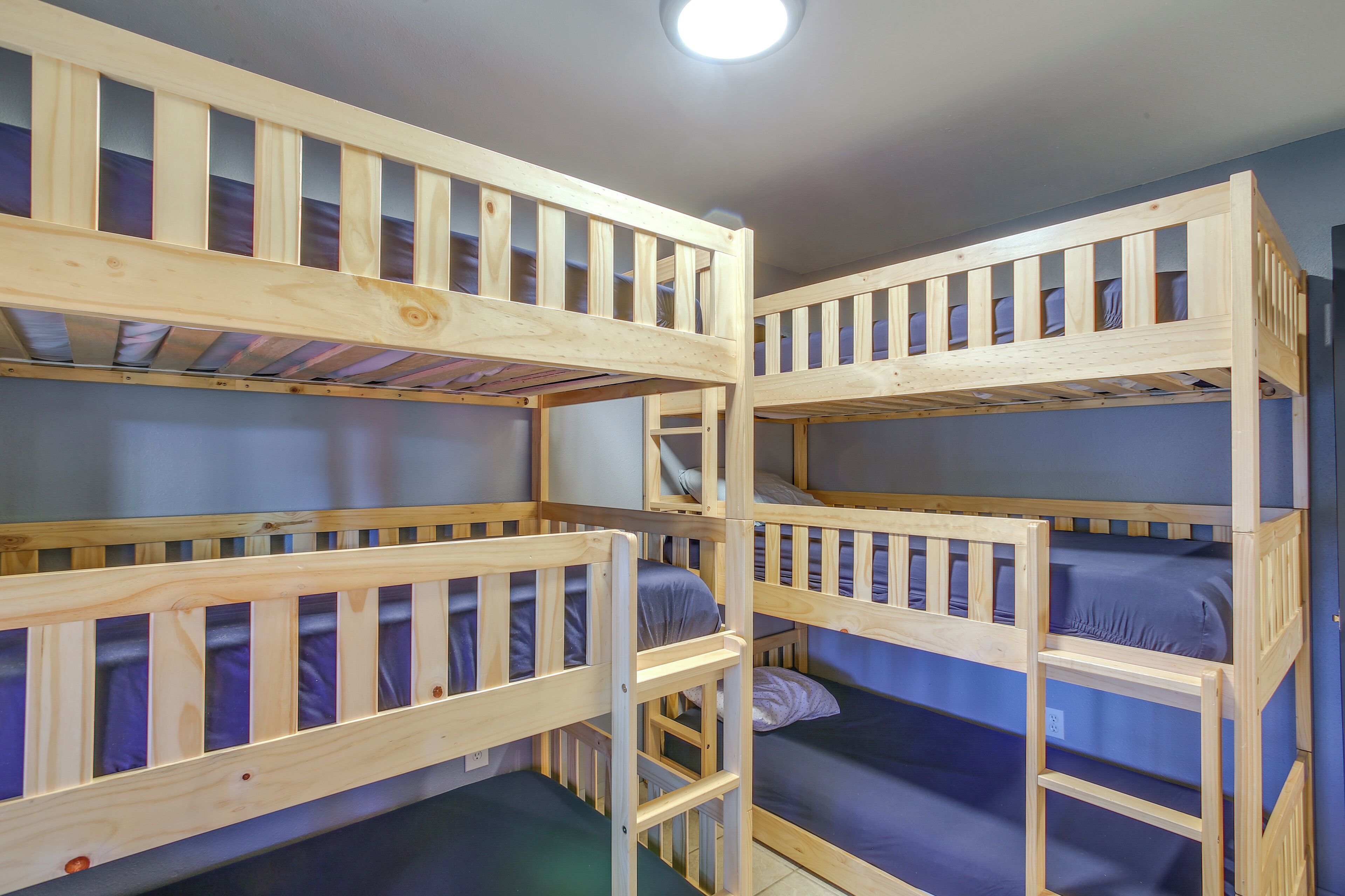 Une chambre avec trois lits superposés en bois, chacun étant équipé de draps bleus.