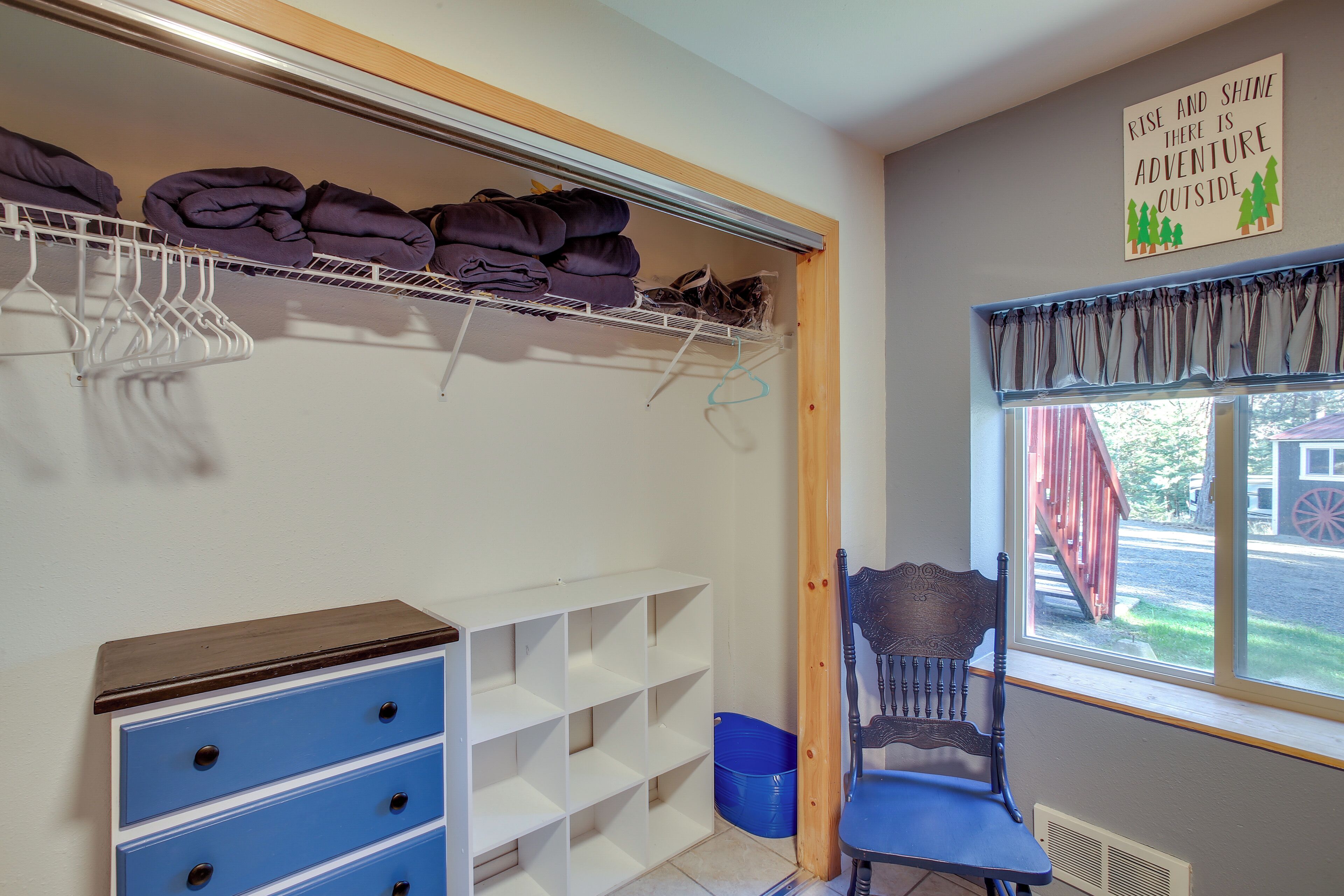 A room with a window, a chair, a shelf with folded clothes, and a sign on the wall.