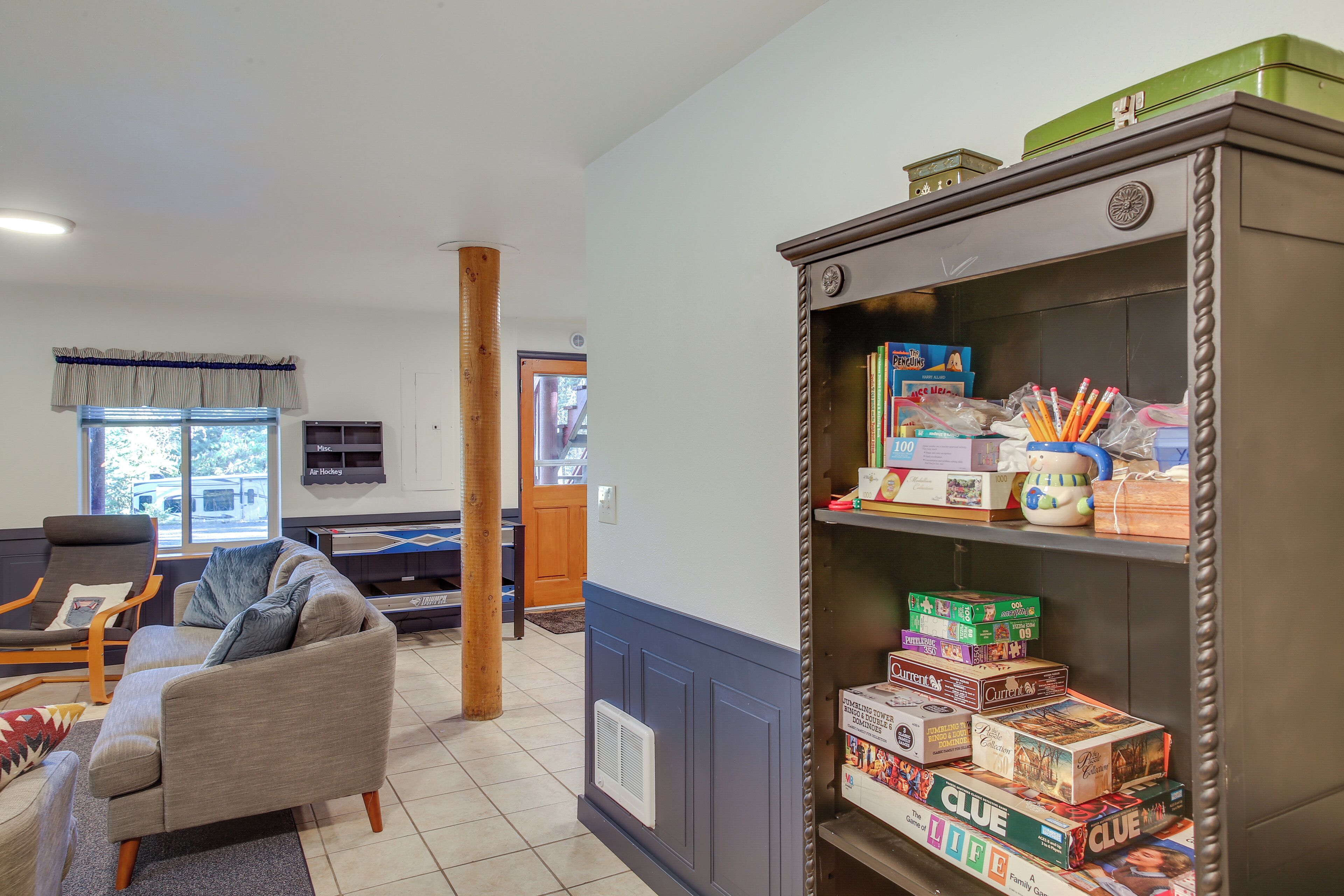 A living room with a sofa, armchair, and a bookshelf filled with board games.