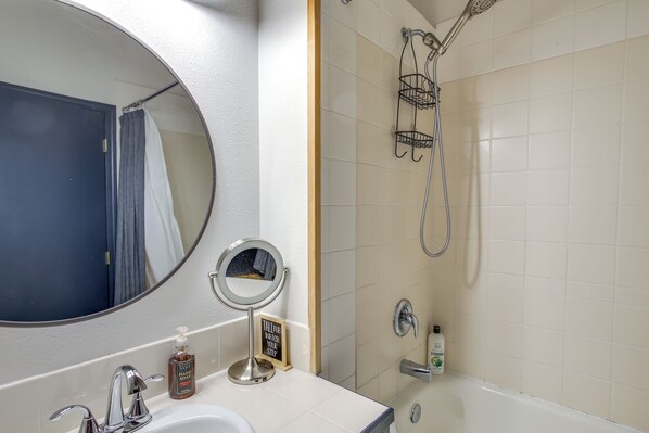 A bathroom with a round mirror, a sink, a handheld showerhead, and a towel rack.