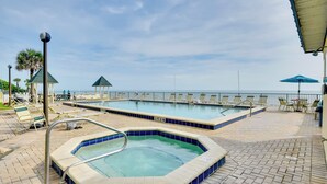 A pool area with a hot tub, lounge chairs, and a view of the ocean.