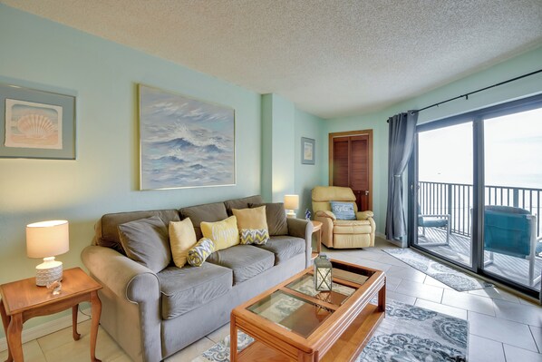 A living room with a sofa, armchairs, a coffee table, and a large window with a view.