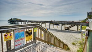A wooden boardwalk leading to a pier with safety signs and a view of the beach.