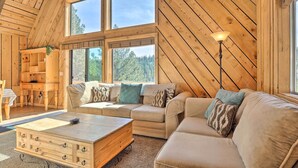 A cozy cabin interior with a large wooden ceiling, a sofa set, a wooden coffee table, and a floor lamp.