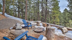 A forested area with a fire pit, wooden benches, and a stone structure.