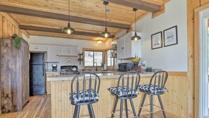 A kitchen with wooden cabinets, a central island with bar stools, pendant lighting, and framed artwork on the wall.
